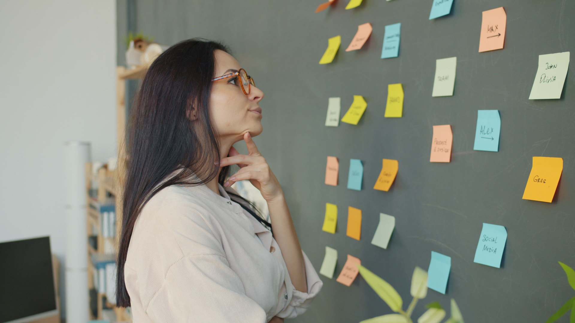 Une collaboratrice organise son travail devant un mur de post-it colorés